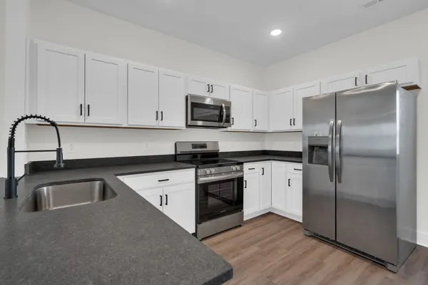 a kitchen with granite countertop a refrigerator a sink dishwasher a stove and white cabinets with wooden floor