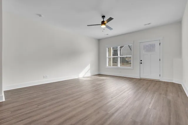 an empty room with wooden floor ceiling fan and window