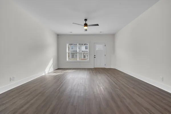 an empty room with wooden floor ceiling fan and windows