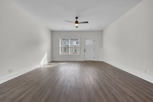 an empty room with wooden floor ceiling fan and windows