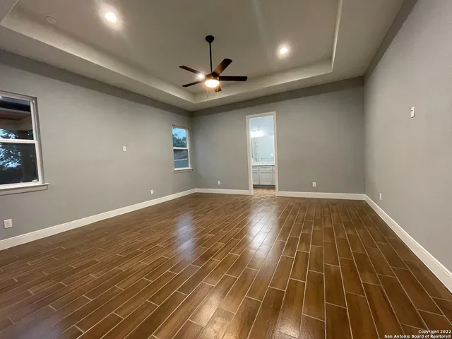 a view of an empty room with wooden floor and a ceiling fan
