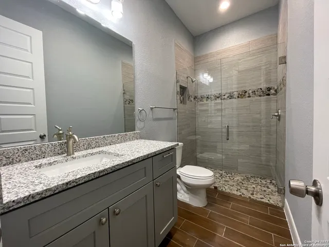 a bathroom with a granite countertop sink a toilet a mirror and shower