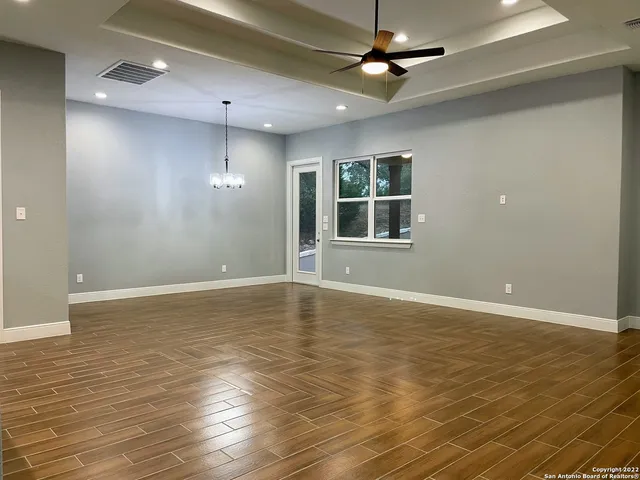an empty room with wooden floor chandelier fan and windows