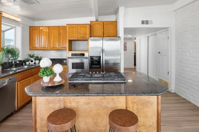 a kitchen with kitchen island granite countertop wooden cabinets a refrigerator a stove and a sink