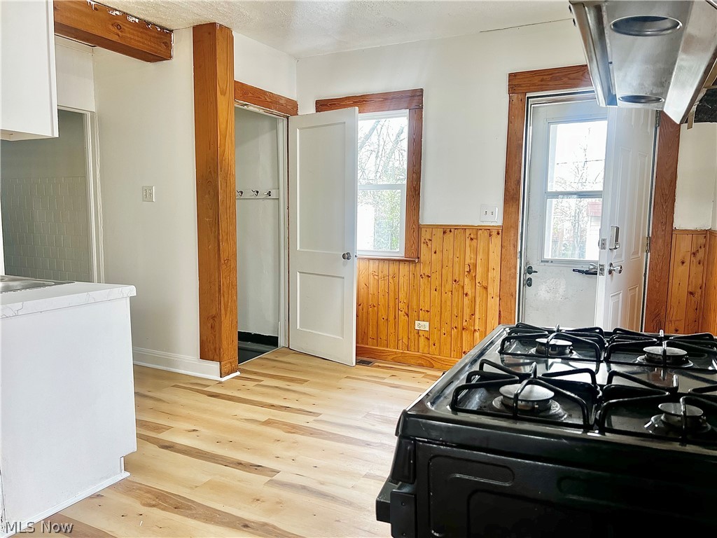 67 Forbes Road Bedford, OH 44146 - Photo 7 of 20 Kitchen with range hood, black range with gas stovetop, wooden walls, light wood-style flooring, and wainscoting