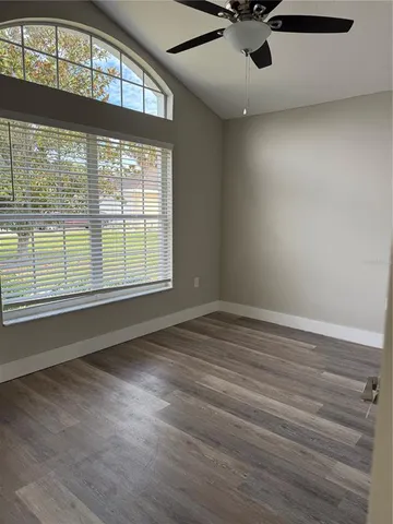 an empty room with wooden floor fan and windows