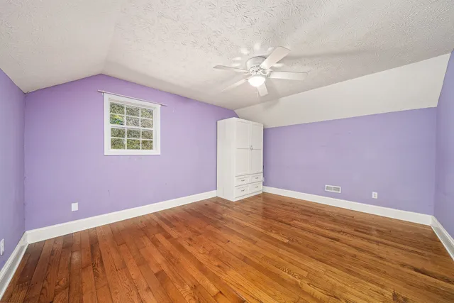 a view of an empty room with chandelier fan and wooden floor