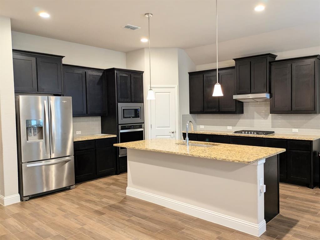 1140 Knightsbridge Road Argyle, TX 76226 - Photo 2 of 13 The kitchen features dark cabinetry, granite countertops, a stainless steel refrigerator, and built-in stainless steel appliances