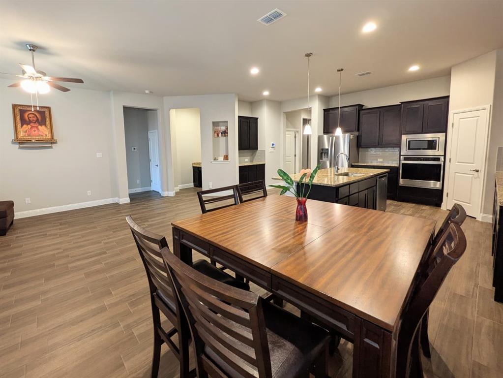 1140 Knightsbridge Road Argyle, TX 76226 - Photo 3 of 13 Open concept living area featuring wood-look tile flooring, a dining area with a wooden table and chairs, and a kitchen with dark cabinetry and stainless steel appliances