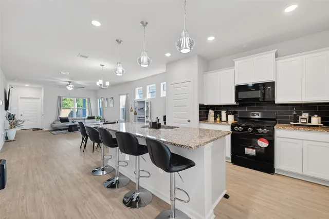 a kitchen with stainless steel appliances kitchen island granite countertop a stove top oven a sink a dining table and chairs with wooden floor