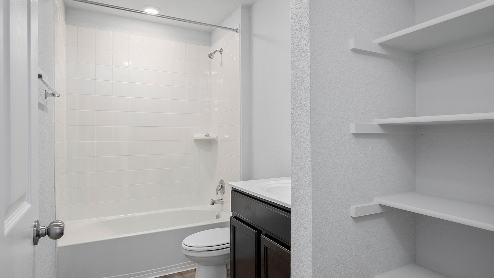 1403 Victory Rnch Trail Killeen, TX 76549 - Photo 20 of 22 This bathroom features a bathtub with a shower, white tiled walls, a dark wood vanity with a white countertop and sink, and built-in white shelving