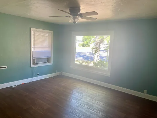 an empty room with wooden floor chandelier and windows