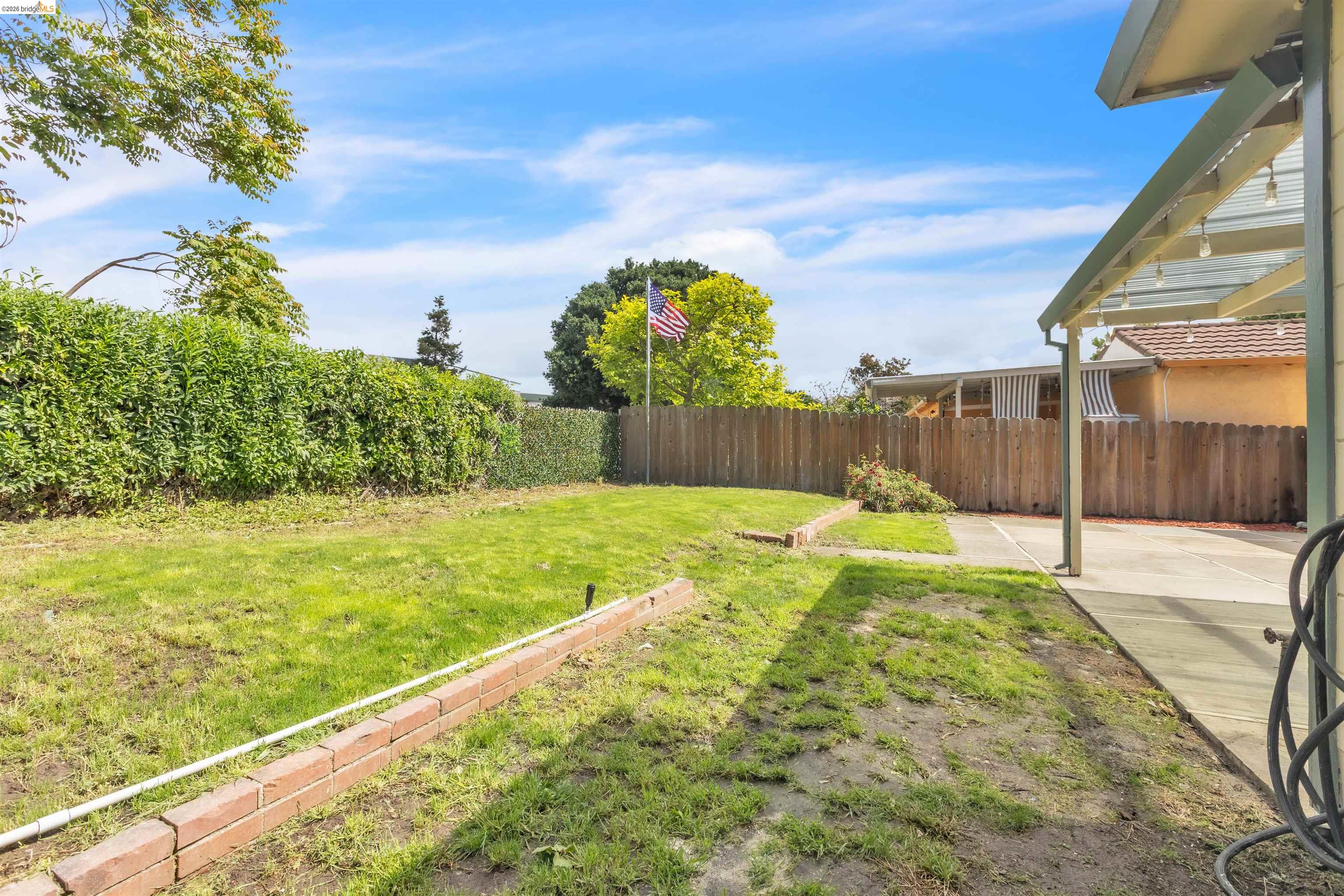 621 Paseo Del Rio San Lorenzo, CA 94580 - Photo 22 of 24 Expansive backyard featuring a concrete patio, a covered patio structure with lighting, a wooden privacy fence, mature perimeter hedging, and brick garden beds