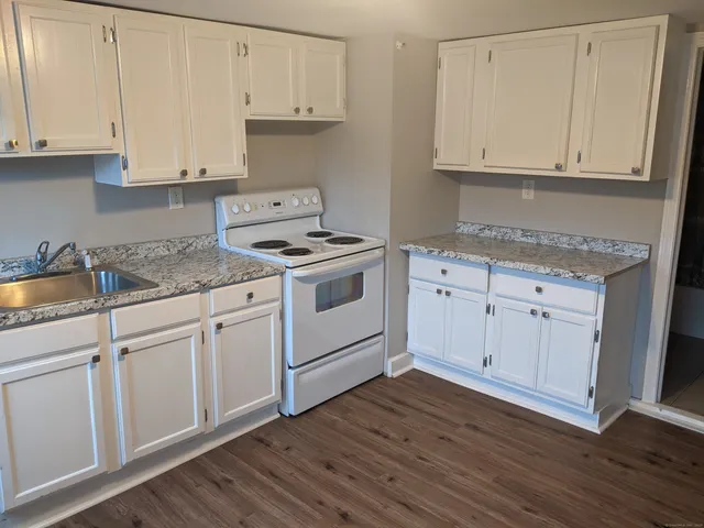 a kitchen with granite countertop white cabinets and a stove with wooden floor
