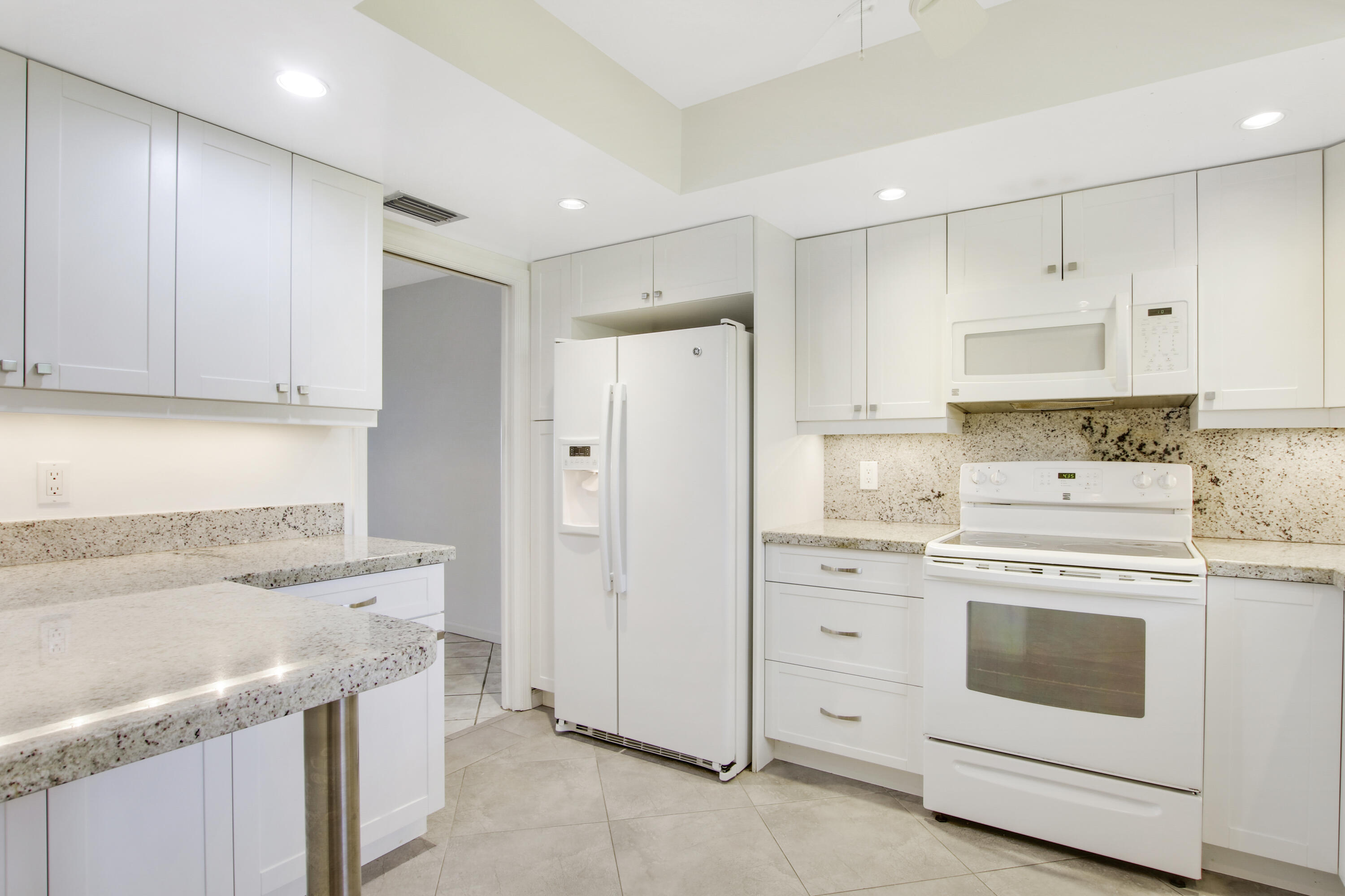 145 Atlantis Boulevard, Unit 105 Atlantis, FL 33462 - Photo 9 of 28 a kitchen with white cabinets and white appliances