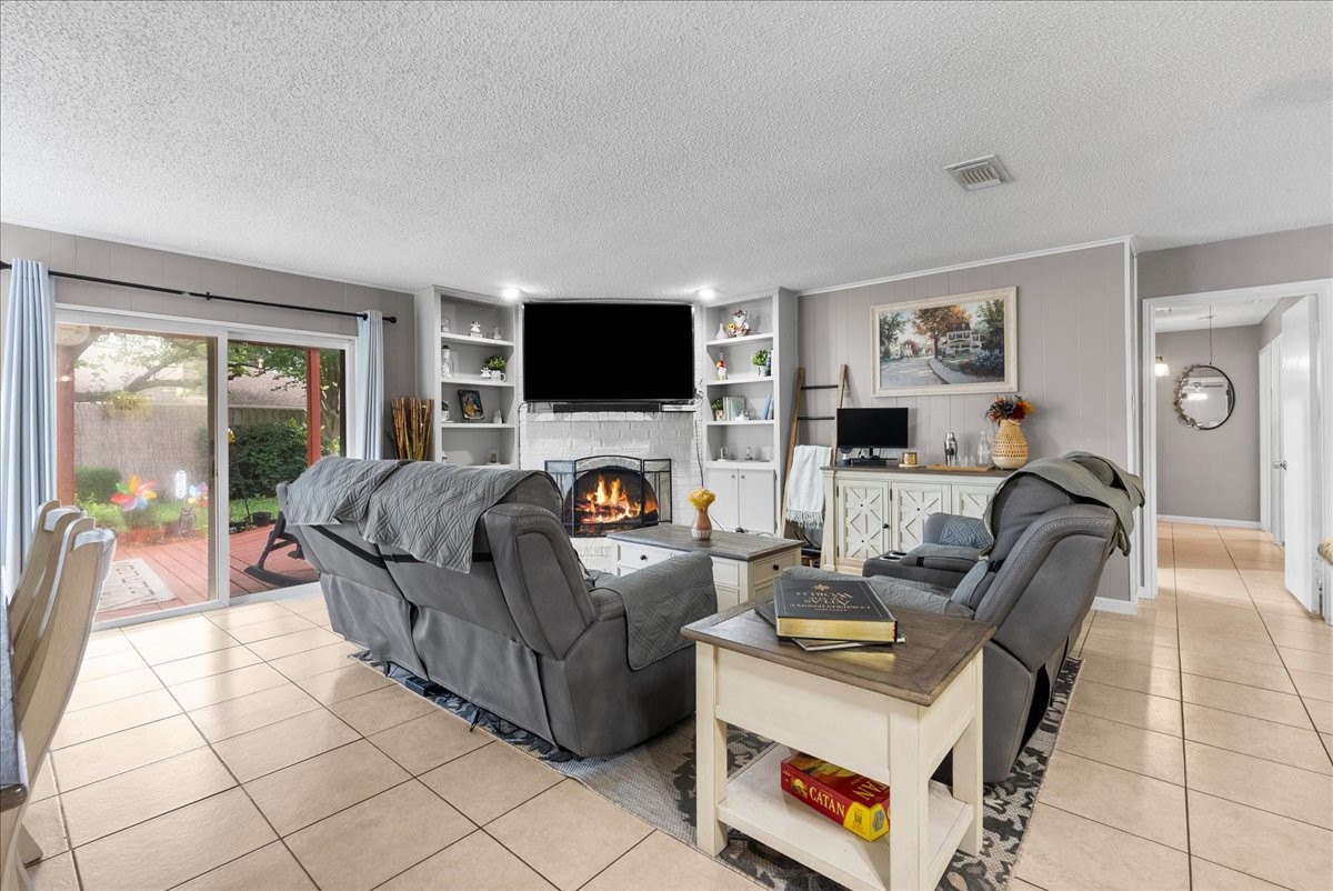 883 Silverpines Road Houston, TX 77062 - Photo 11 of 38 This cozy living room features a tiled floor, a fireplace with built-in shelving, and sliding glass doors leading to a patio. Comfortable seating and a neutral color palette create a welcoming atmosphere.