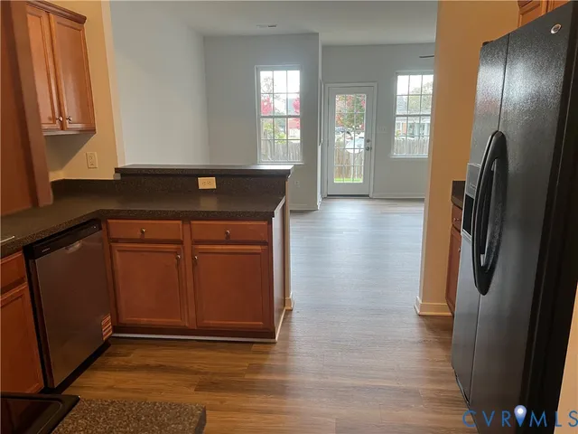a view of a refrigerator in kitchen and an empty room with wooden floor