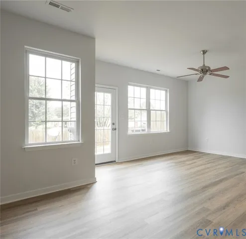 an empty room with wooden floor fan and windows