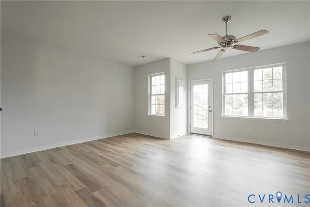 an empty room with wooden floor chandelier fan and windows