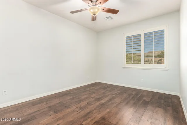 an empty room with wooden floor fan and windows