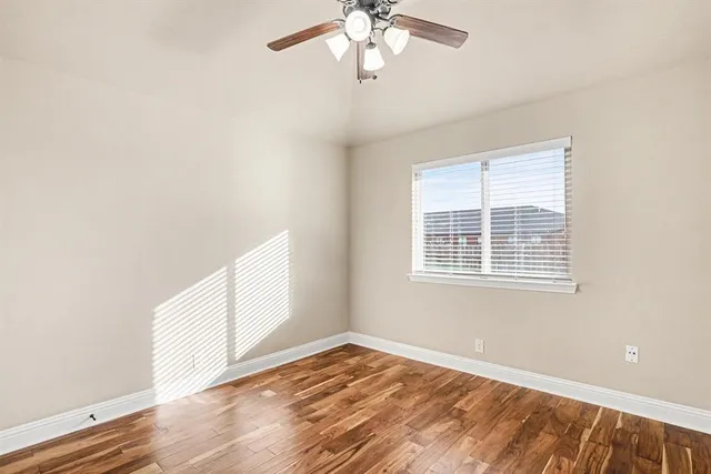 an empty room with wooden floor fan and windows