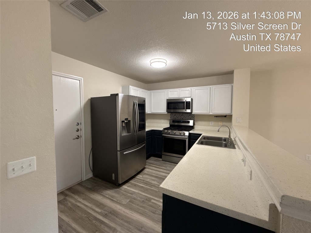5713 Silver Screen Drive Austin, TX 78747 - Photo 2 of 21 Kitchen featuring stainless steel appliances, a peninsula, white cabinetry, light wood-style flooring, and a textured ceiling