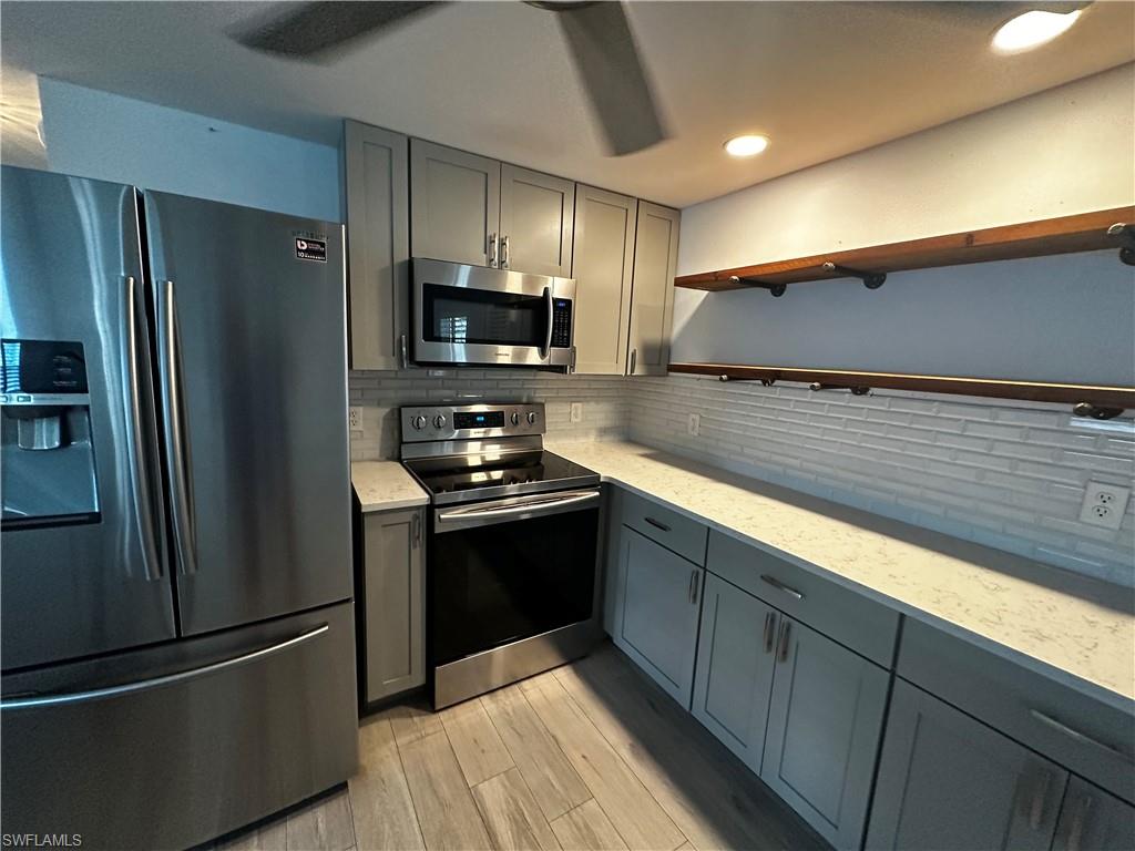 170 Pine Key Lane, Unit 13 Naples, FL 34114 - Photo 33 of 34 Kitchen with stainless steel appliances, gray cabinetry, open shelves, light wood-style floors, and light stone countertops