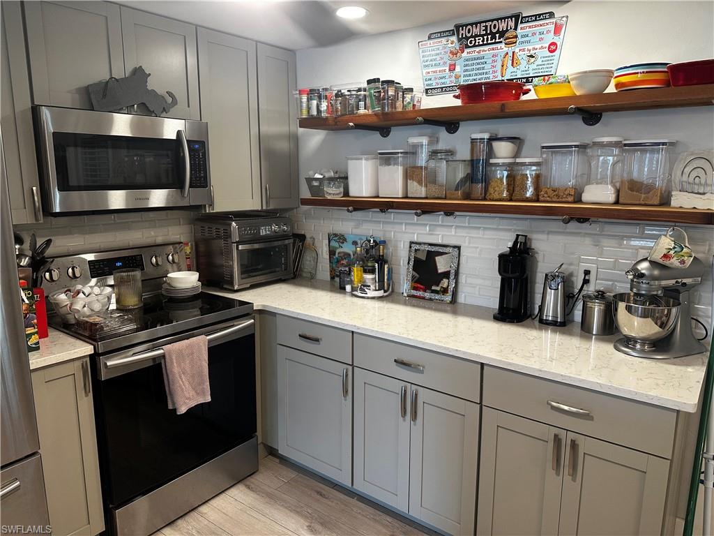 170 Pine Key Lane, Unit 13 Naples, FL 34114 - Photo 8 of 34 Kitchen with gray cabinets, open shelves, stainless steel appliances, and light stone countertops