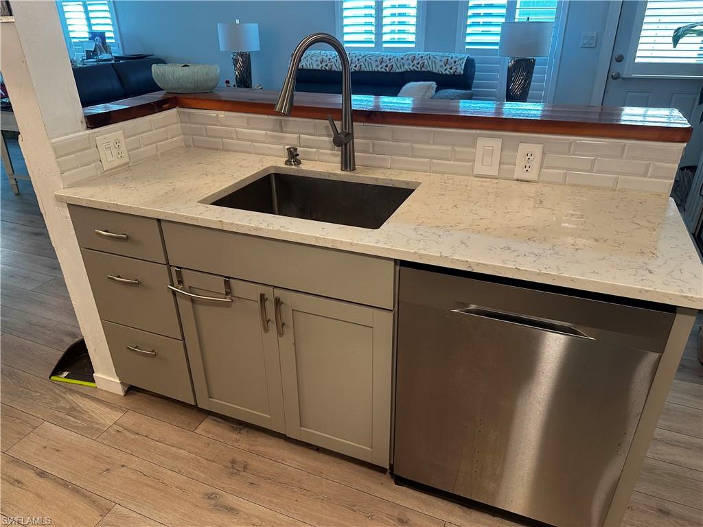 170 Pine Key Lane, Unit 13 Naples, FL 34114 - Photo 9 of 34 Kitchen with stainless steel dishwasher, gray cabinets, light stone counters, light wood-style flooring, and tasteful backsplash