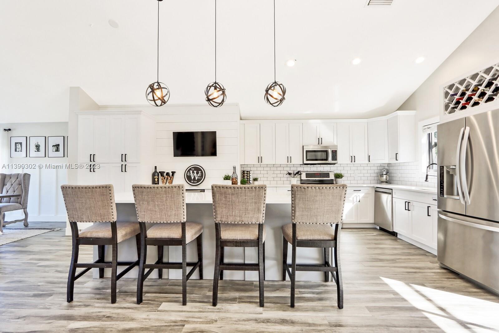 6122 Adams Street Jupiter, FL 33458 - Photo 10 of 59 a kitchen with stainless steel appliances kitchen island granite countertop a dining table chairs and a refrigerator