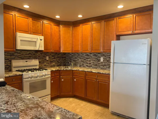 a kitchen with stainless steel appliances granite countertop a refrigerator a sink dishwasher a stove and white countertops with wooden floor