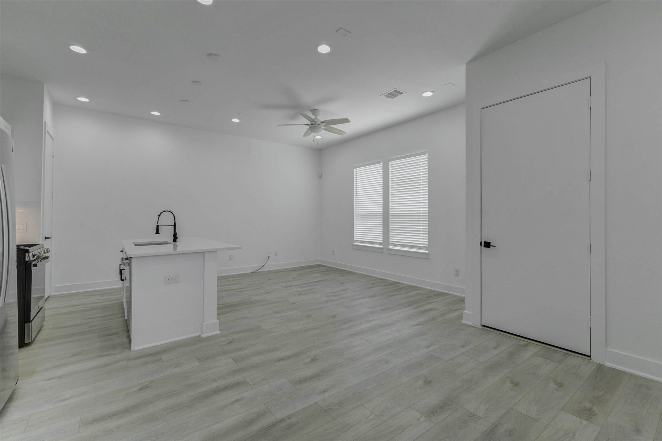 5705 Elysium Street Houston, TX 77091 - Photo 10 of 22 Open-concept living area with light wood-look flooring, tall ceilings, recessed lighting, ceiling fan, and a sleek kitchen island. The spacious layout connects the kitchen, dining, and living areas with a clean modern flow, offering flexible space for entertaining, relaxing, and everyday living in a bright neutral setting.