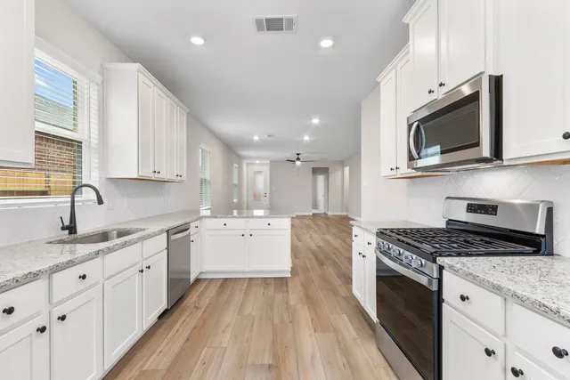 a kitchen with stainless steel appliances granite countertop a stove top oven a sink dishwasher and white cabinets with wooden floor