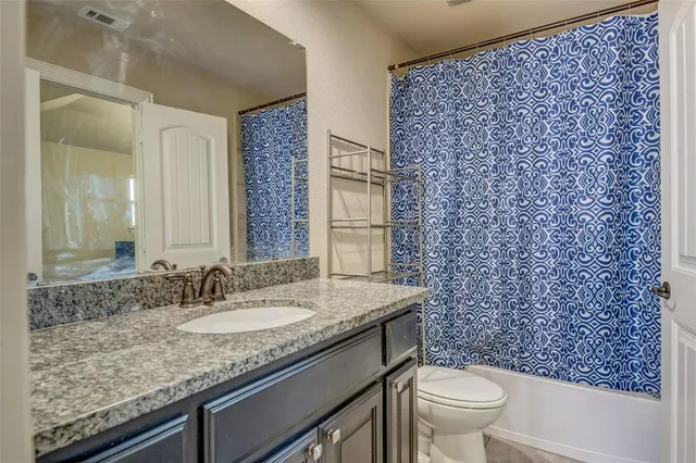 a bathroom with a granite countertop sink a toilet a mirror and shower curtain