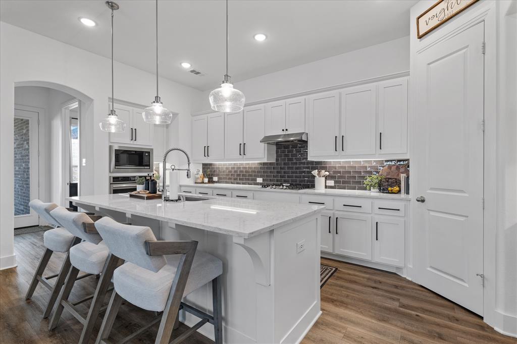 Kitchen with arched walkways, a breakfast bar, a kitchen island with sink, white cabinets, and dark wood-style flooring