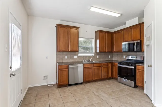 a kitchen with stainless steel appliances granite countertop a stove top oven a sink dishwasher a refrigerator and a microwave oven