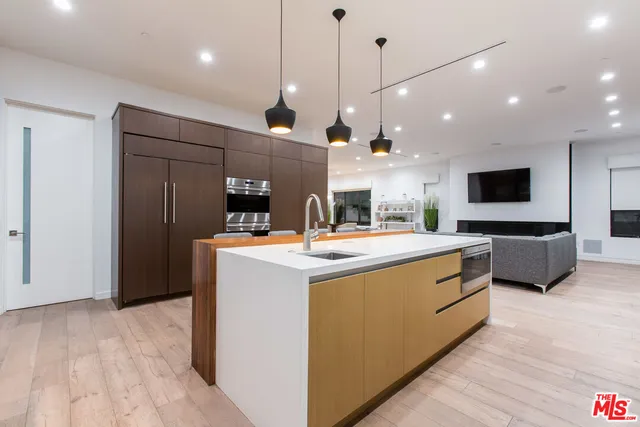 a view of a kitchen with kitchen island a counter top stainless steel appliances and a ceiling fan