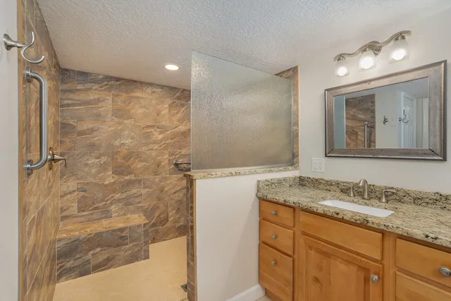 a bathroom with a granite countertop sink a mirror and a shower