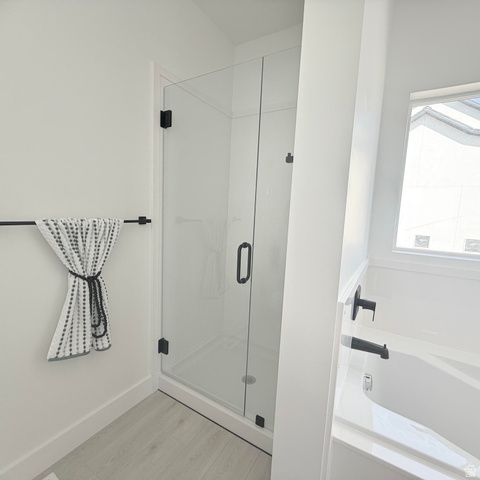 5777 West 4100 South Hooper, UT 84315 - Photo 24 of 41 Modern bathroom featuring a frameless glass shower enclosure with matte black hardware, a pristine white tub with matte black fixtures, light-toned wood-finish flooring, and a white baseboard trim