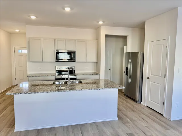 a large kitchen with stainless steel appliances granite countertop a stove a sink a refrigerator and a granite counter tops with wooden floors