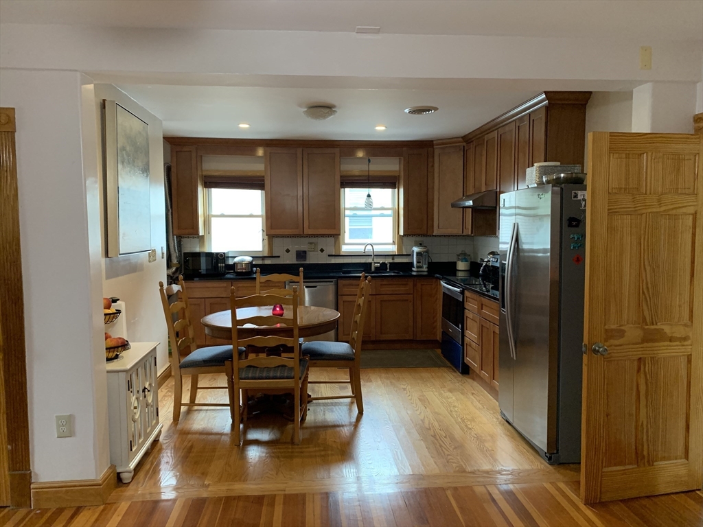 23 Lafayette Street, Unit 23 Arlington, MA 02474 - Photo 2 of 18 a kitchen with stainless steel appliances granite countertop a refrigerator a stove a sink a dining table and chairs with wooden floor