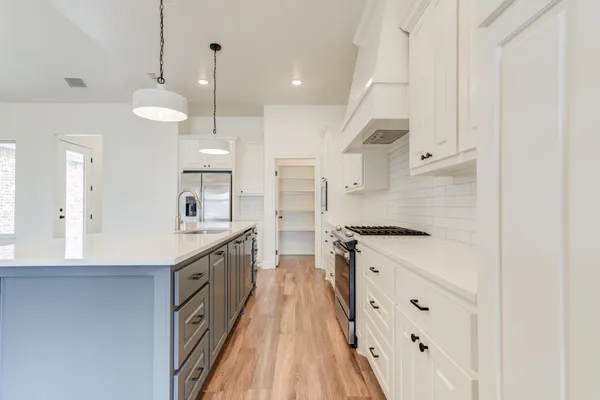 a large kitchen with granite countertop a stove a sink dishwasher and a refrigerator with wooden floor