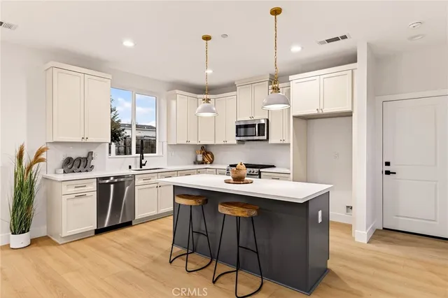 a kitchen with stainless steel appliances granite countertop a sink a stove a refrigerator and white cabinets with wooden floor