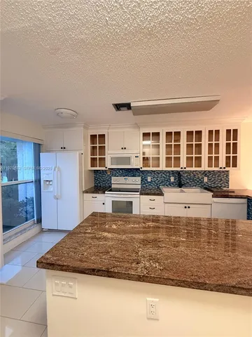 a large white kitchen with large trees and a potted plant
