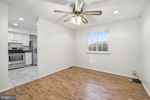 an empty room with wooden floor a ceiling fan and kitchen view
