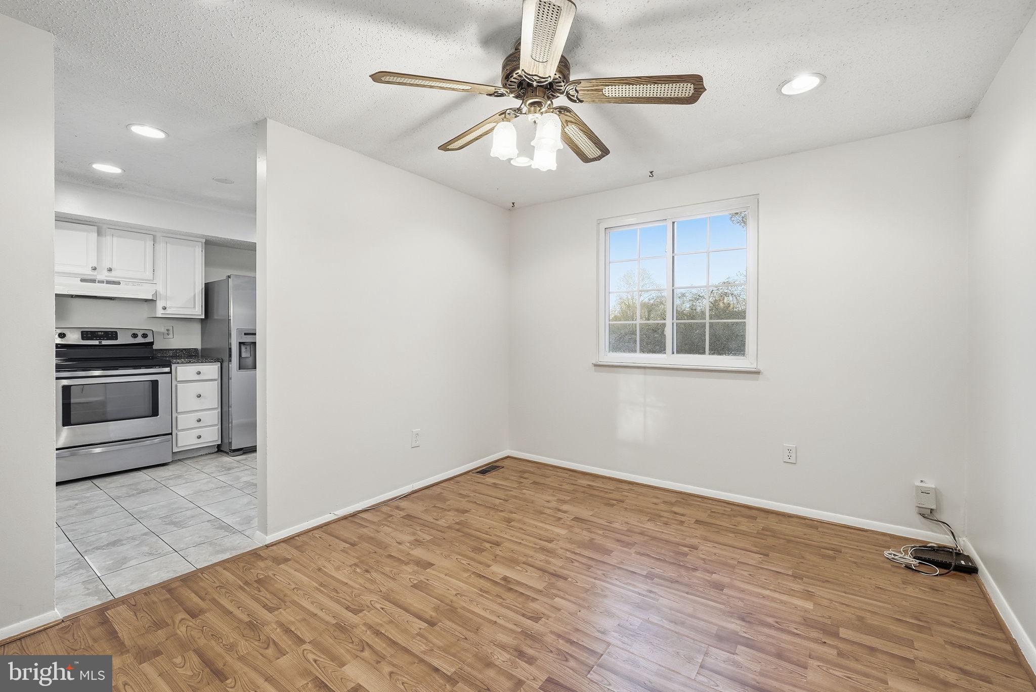 9804 Gabon Court Burke, VA 22015 - Photo 11 of 30 an empty room with wooden floor a ceiling fan and kitchen view