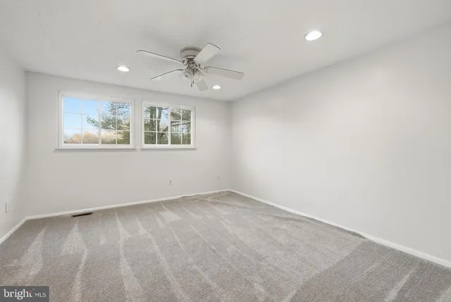 an empty room with wooden floor ceiling fan and windows