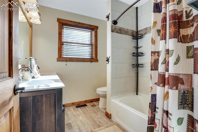 405 Cochetopa Road Florissant, CO 80816 - Photo 17 of 28 Newly Updated Main Bathroom with tile wood planked flooring, low flush water saving toilet, bronze fixtures, double sink with smooth countertops, vanity with barn door style doors and ample storage, tile surround shower/tub with wood plank tile accents and views of the trees!