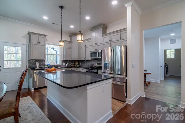 a kitchen with stainless steel appliances granite countertop a refrigerator a sink dishwasher a stove and a dining table with wooden floor