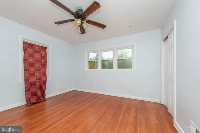 an empty room with wooden floor chandelier fan and windows
